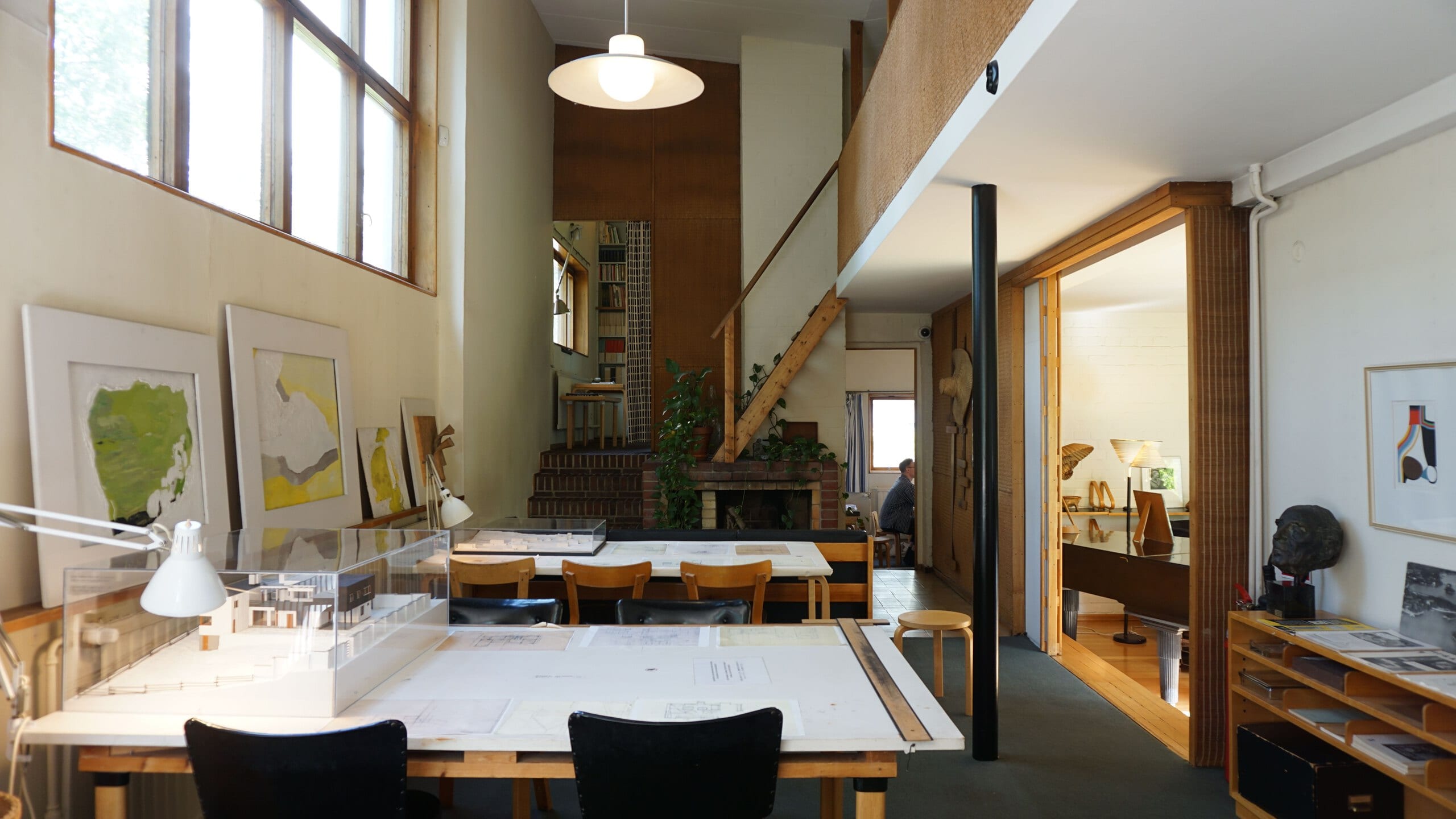 A design studio with drafting tables, a scale model and framed drawings under daylight
