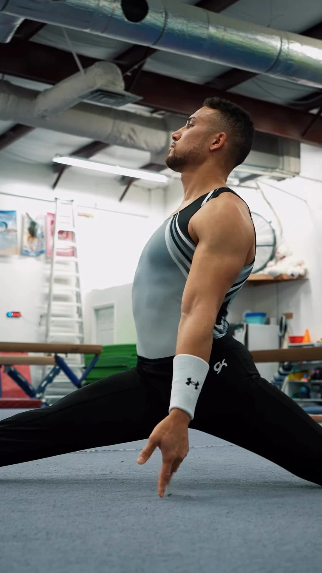 Frame from an athlete film: a gymnast in a sleeveless top holds a split stretch in a training gym