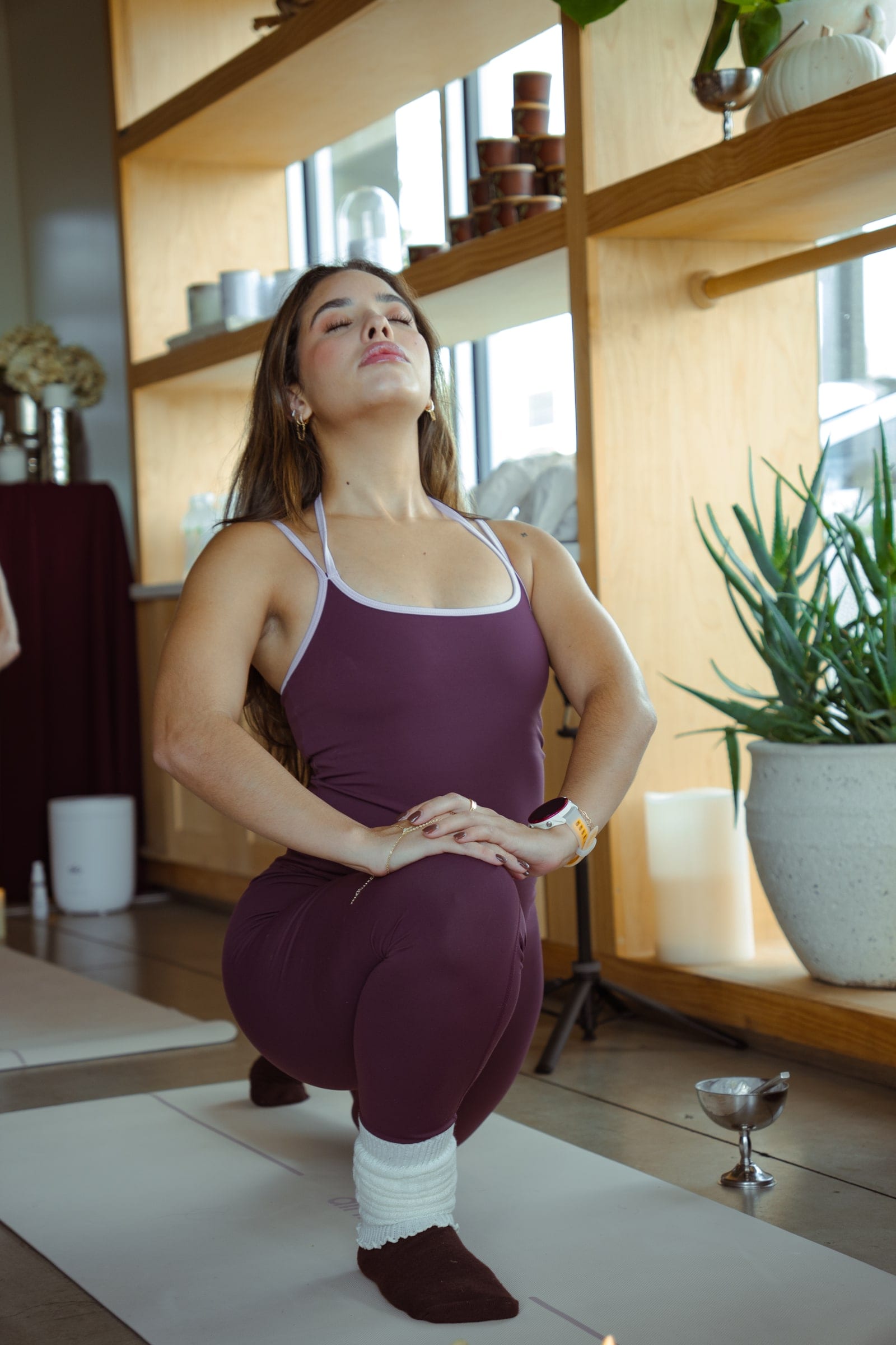 A woman in a low lunge stretch with her eyes closed in a sunlit wellness space