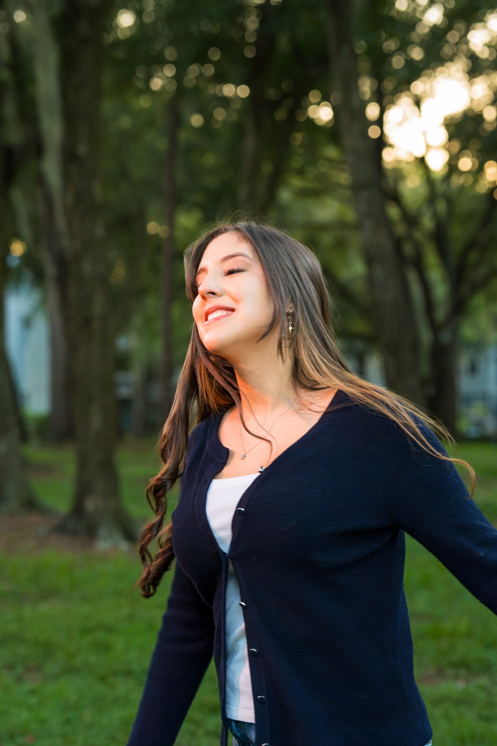 A smiling subject turns with her hair in motion in a tree-lined park at golden hour