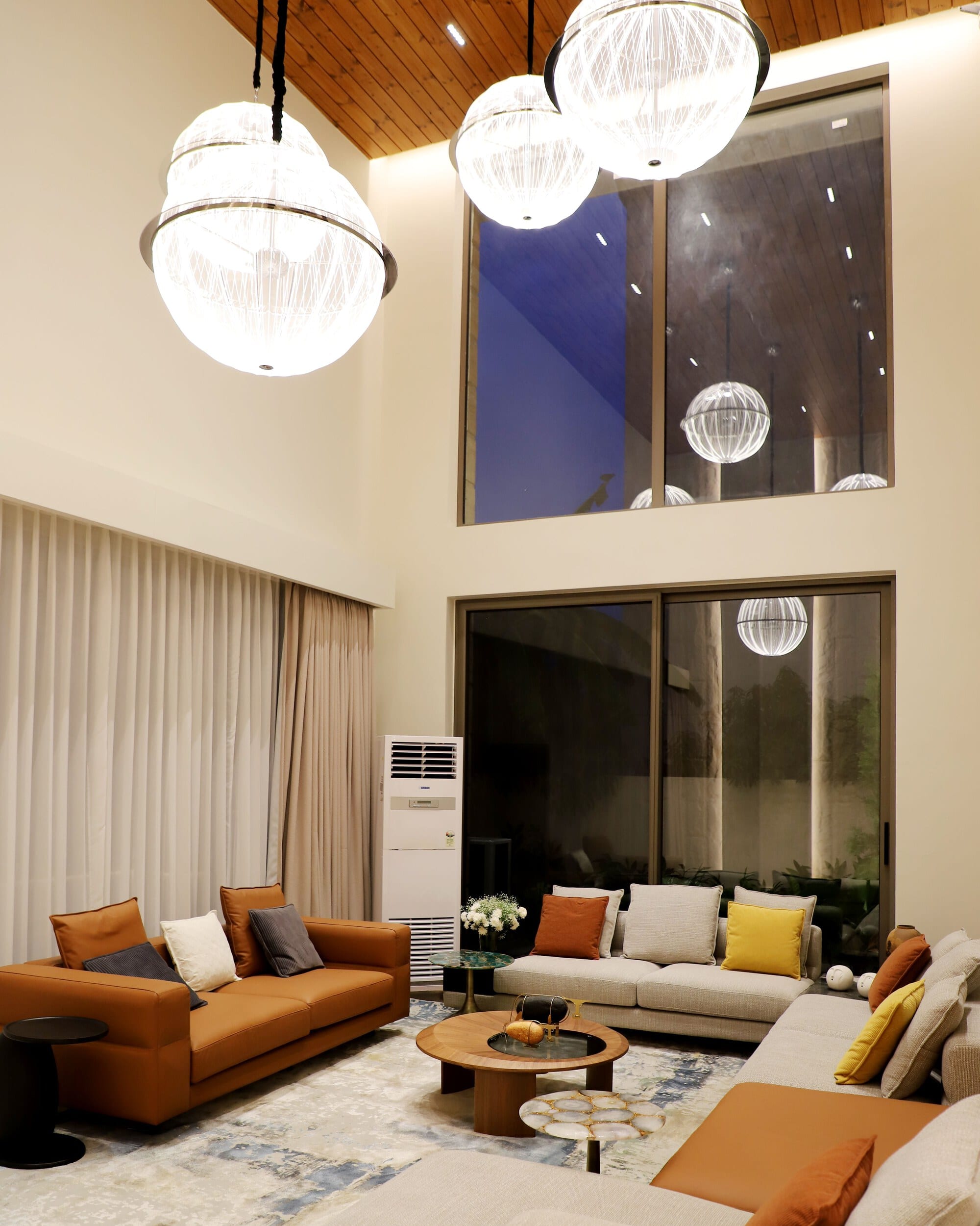 A double-height living room with tall windows, pendant globes and orange sofas