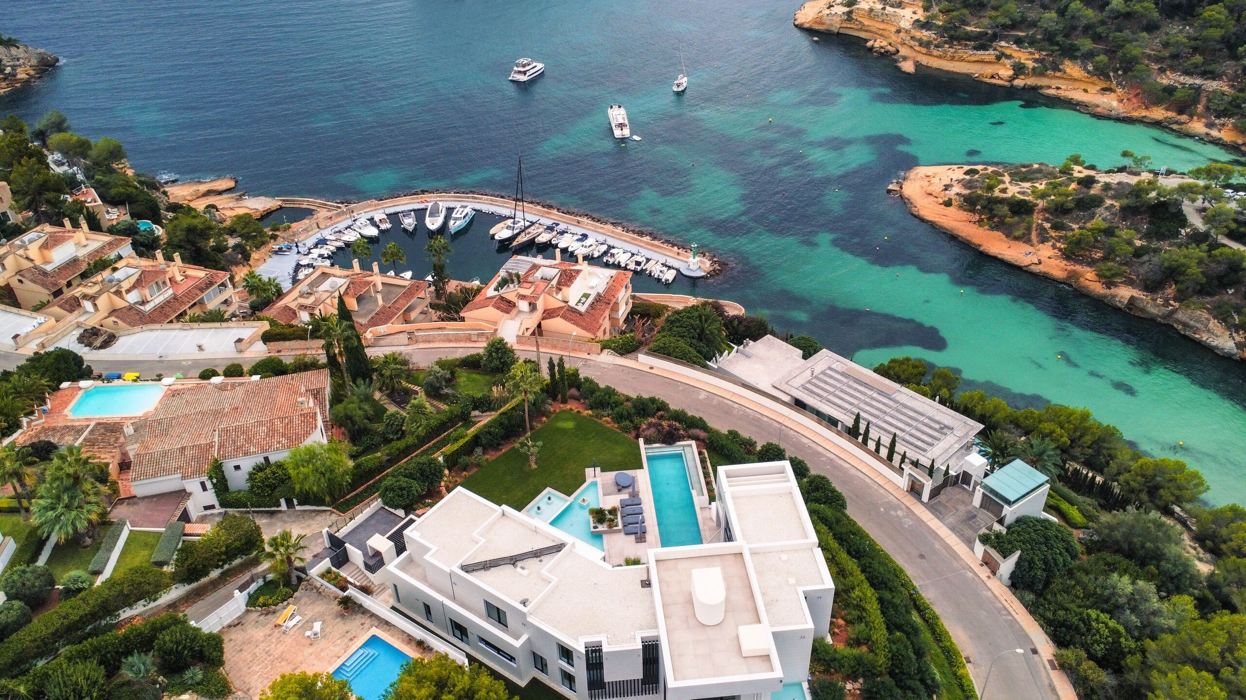 Aerial view of a hillside villa and pools above a marina and a turquoise bay