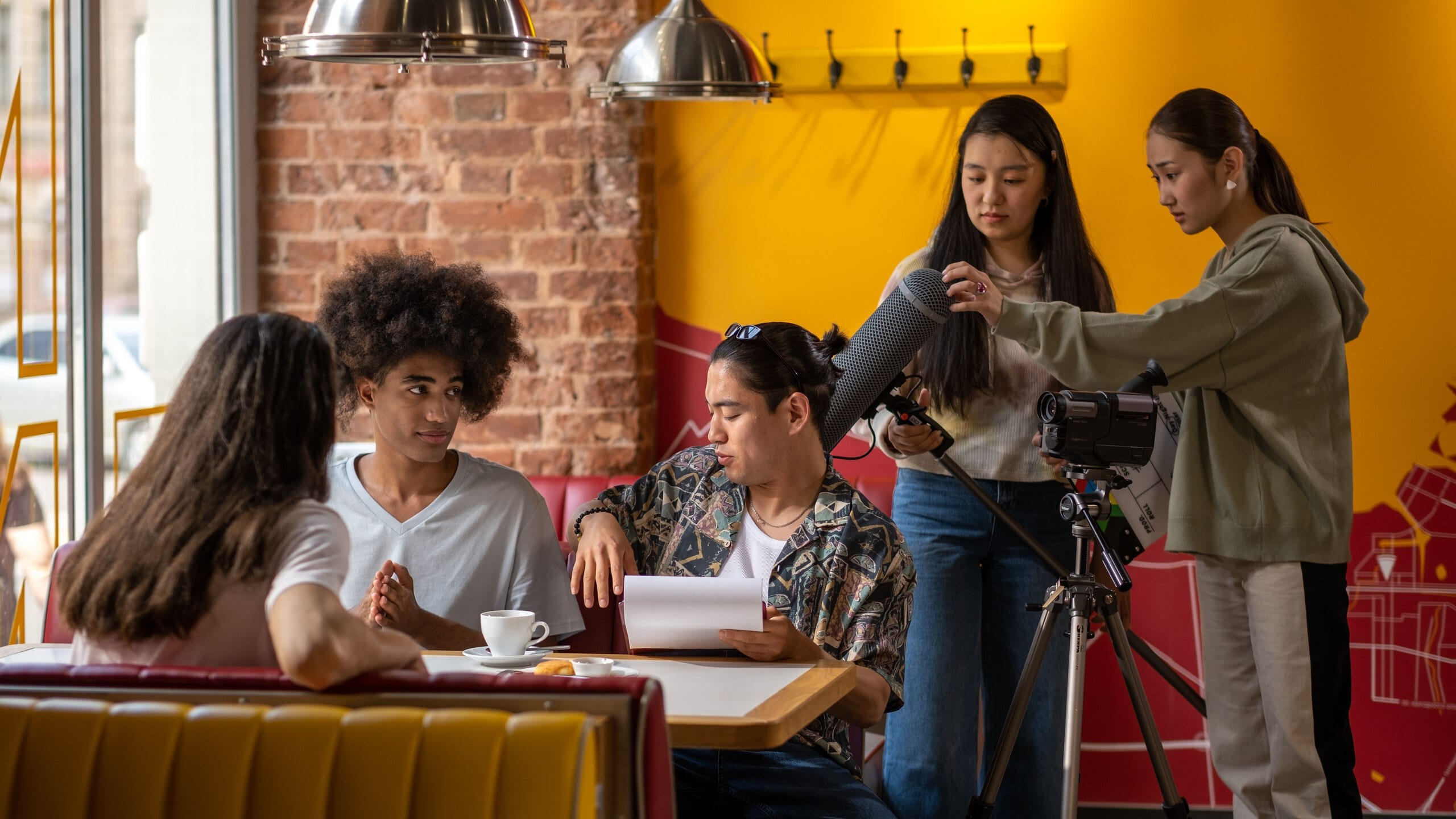 A small film crew recording three people seated in a cafe booth